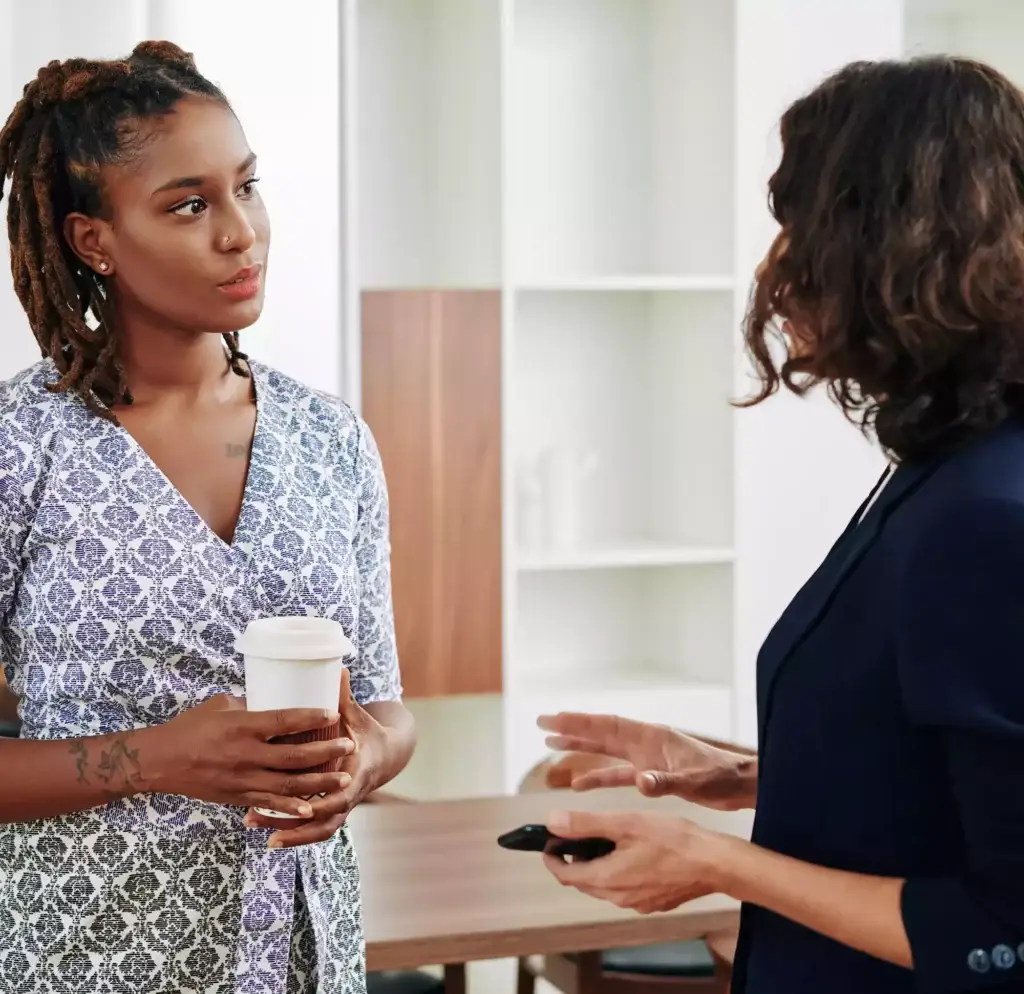 Two female social workers chatting with a cup of coffee in an office