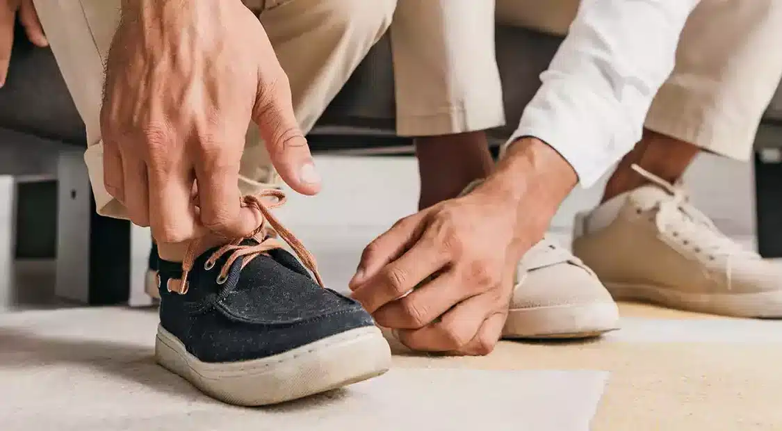 Man tying shoe lace with carer next to them