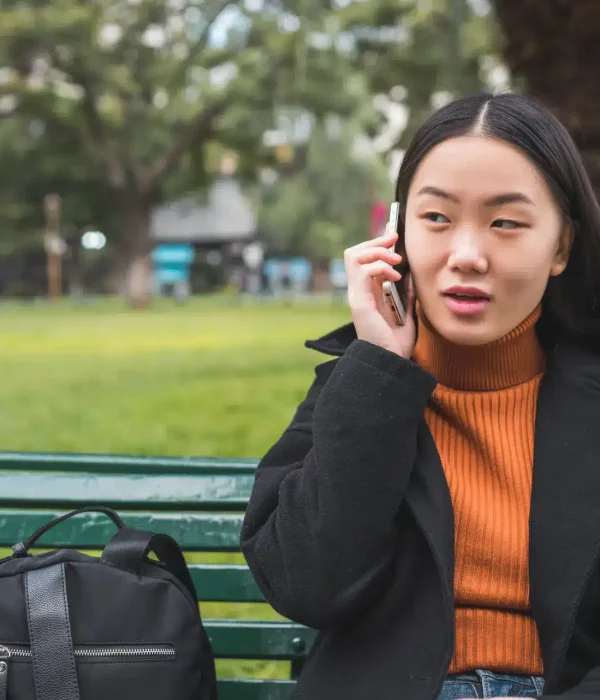 Social Worker chatting on the phone, sat in the park on a bench