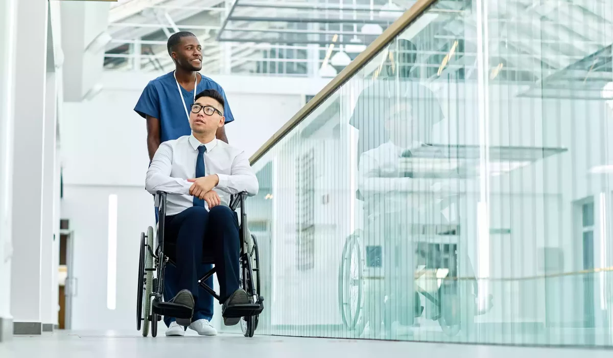 Carer wheeling man with disability down the hall of a hospital